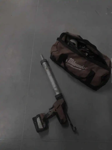 Aku vrtačka s taškou na nářadí na šedé podlaze.