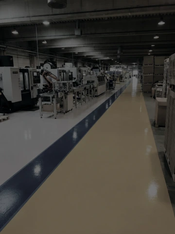 Výrobní hala s řadou průmyslových strojů a označenou bezpečnostní zónou na podlaze.