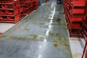 Zaplavena podlaha v průmyslové hale s červenými regály na obou stranách.