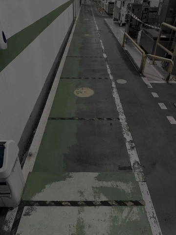 Průmyslová chodba se zelenými pruhy a kovovým zábradlím, podél zdi koš.