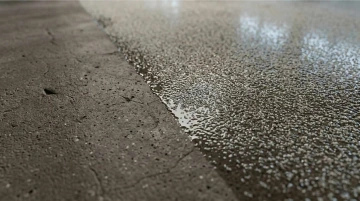 Mokrá betonová podlaha s jemnými prasklinami a lesklým povrchem.