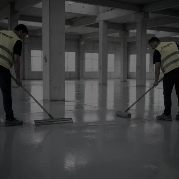 Dva dělníci nanášejí epoxidovou podlahu v prázdné průmyslové hale.