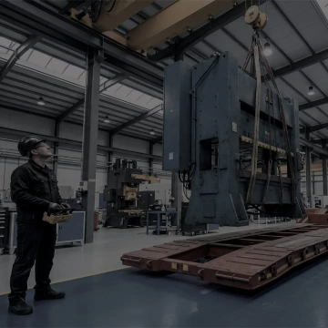 Pracovník řídící jeřáb s velkým strojem v tovární hale.