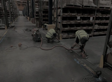 Dělníci v reflexních vestách používají nářadí na úpravu betonové podlahy ve skladu.