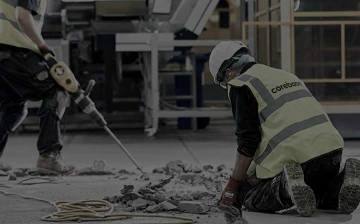 Dva stavební dělníci s helmami a reflexními vestami rozbíjejí betonovou podlahu.