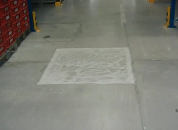 Světlá betonová podlaha v průmyslovém skladu s červenými plastovými boxy na paletách vlevo.