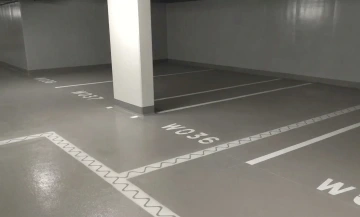 Podzemní parkoviště s očíslovanými parkovacími místy a bílou sloupovou konstrukcí.