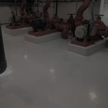 Čerpadla a potrubí v průmyslové hale s lesklou epoxidovou podlahou.