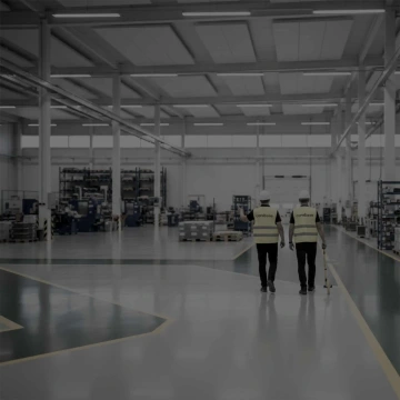 Dva pracovníci v reflexních vestách procházejí průmyslovou halou.