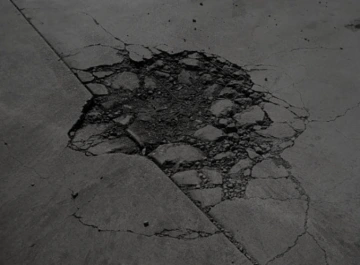 Prasklina v asfaltu s poničenou a rozpadlou strukturou povrchu.